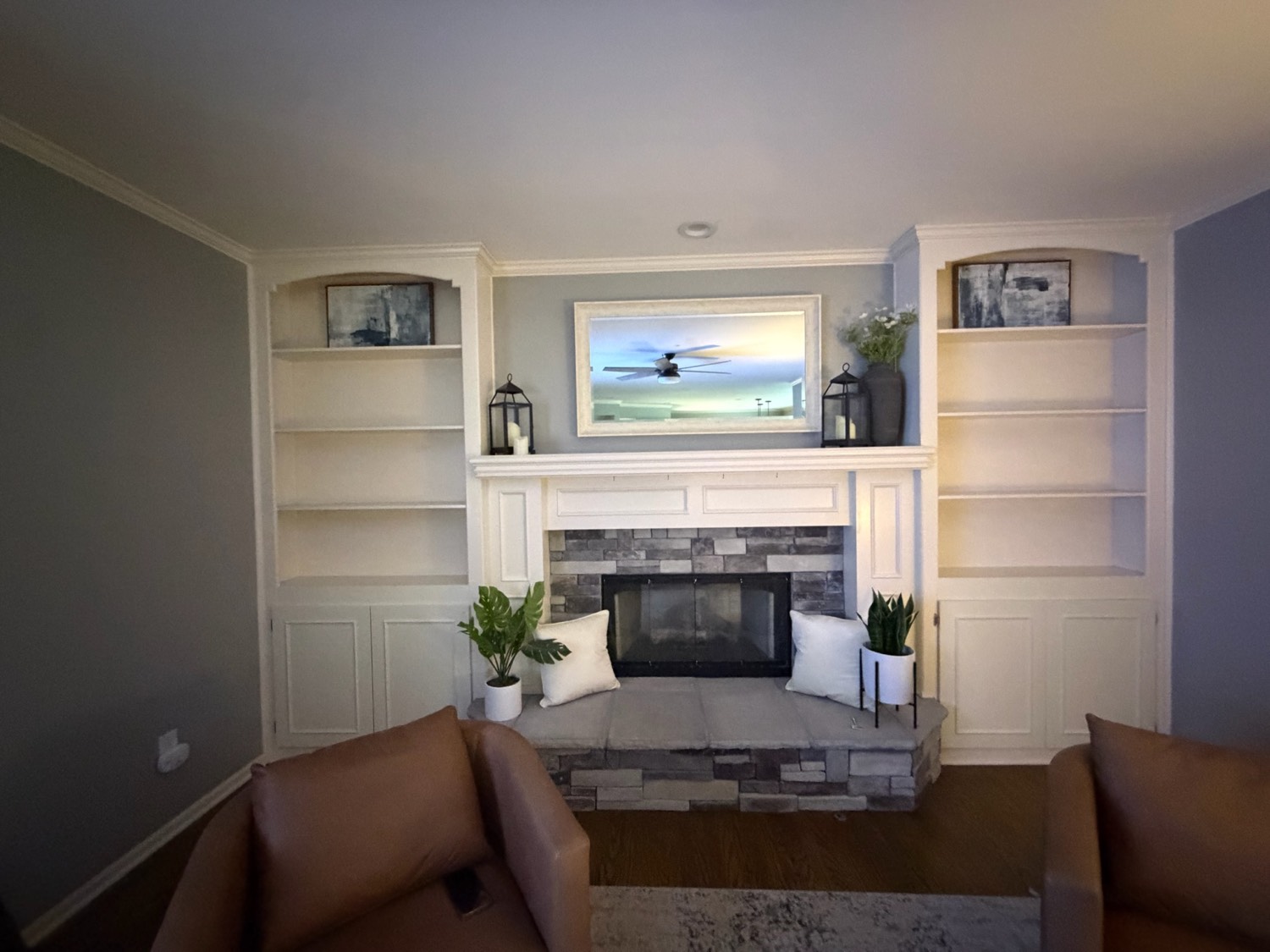 Completed living room with white built-in shelving and cabinets flanking a stone fireplace and painted mantel